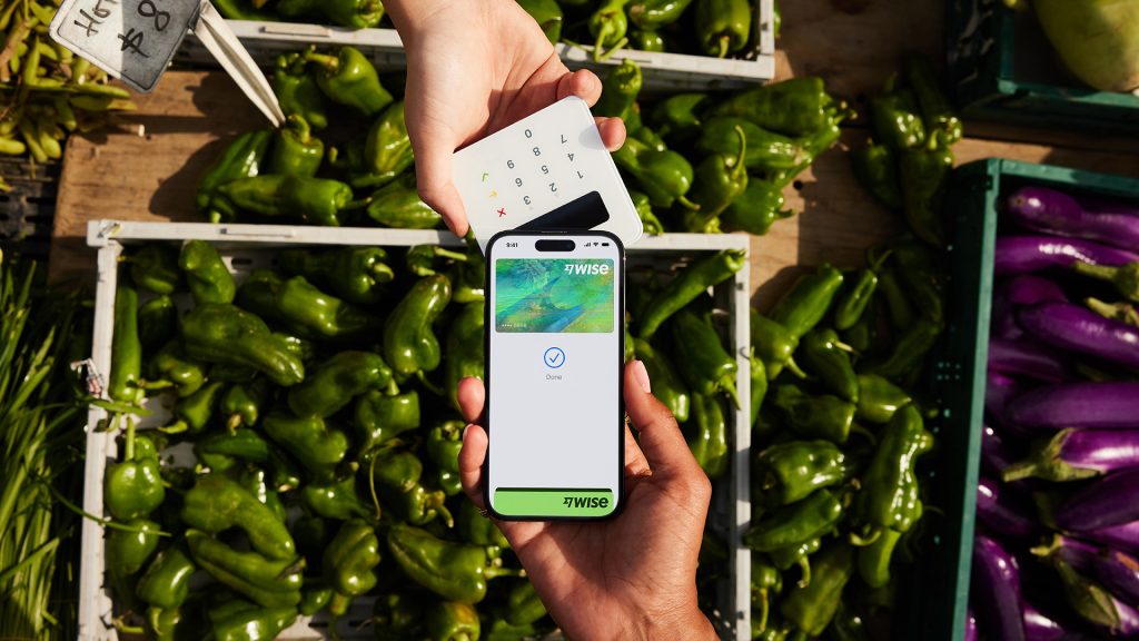 A photo showing a person using their iPhone to pay for vegetables using a Wise debit card connected to Apple Pay