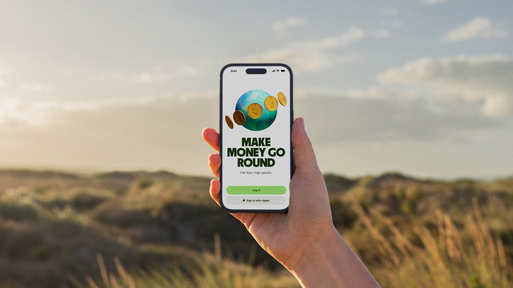 Persons hand, holding an iPhone dieplaing the Wise banking log in screen in front of a field.