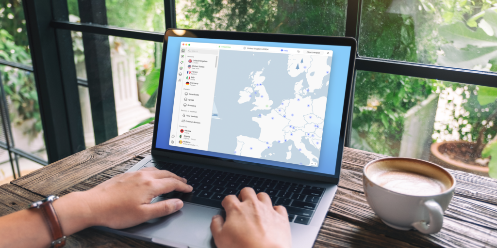 Stock image of a laptop in a cafe with a natural green background. The laptop screen shows the NordVPN macOS app.